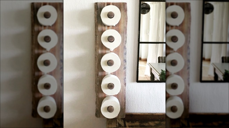 A wooden peg board holding toilet paper rolls