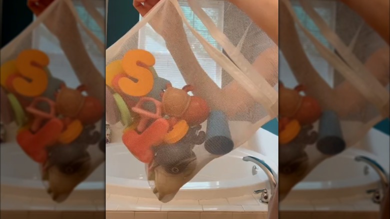Bath toys in a white laundry bag near bathtub