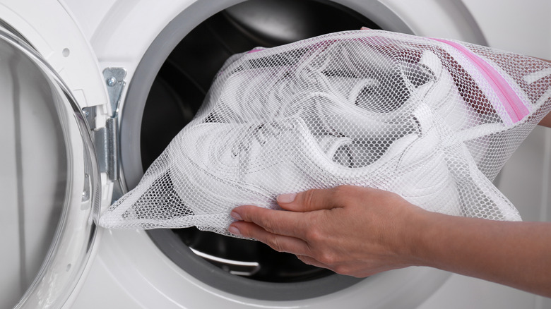 Hands putting white shoes in a mesh laundry bag in the washer