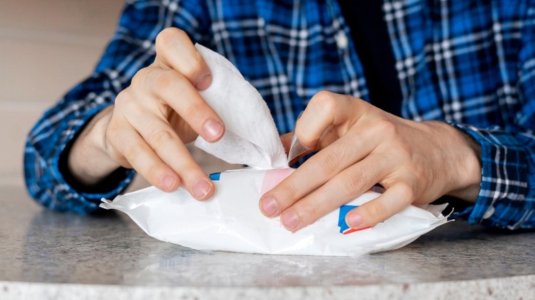 Person removing disinfectant wipe from pack on granite countertop.