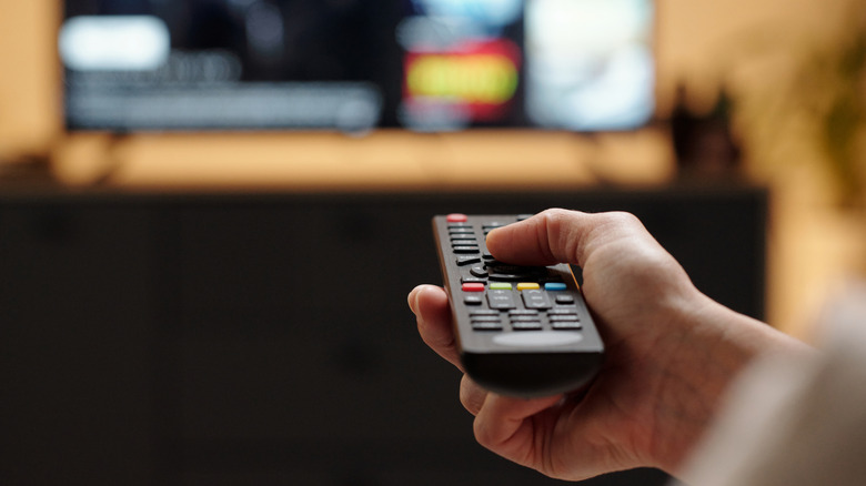 A hand pointing a remote control at the TV.