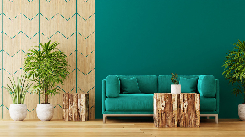 An emerald sofa against an emerald wall behind a wooden coffee table with plants