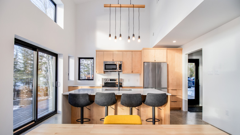 A kitchen all done in a light oak finish with dark gray barstools and an Edison bulb ceiling fixture