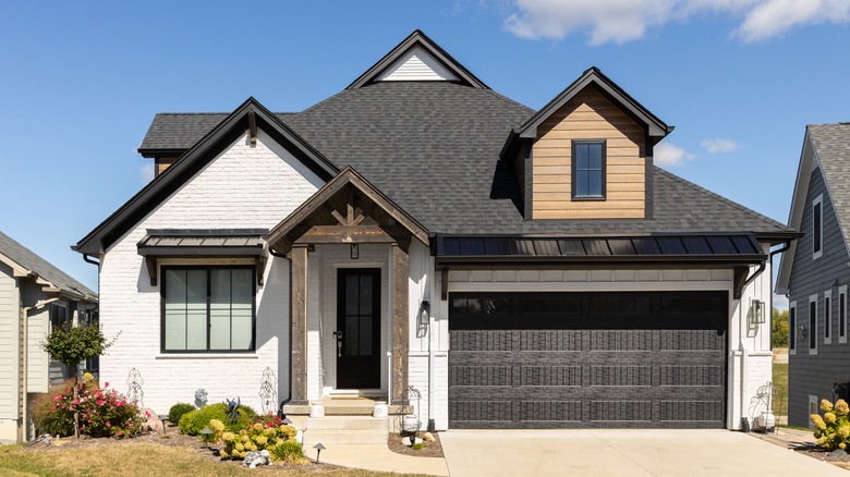 A home with painted white brick and a black roof and garage door