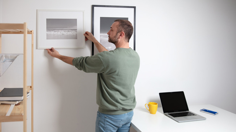 A person hanging framed photographs on an office wall