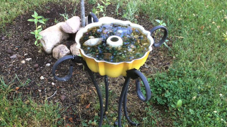 A yellow cake pan used as a bird bath on a stand