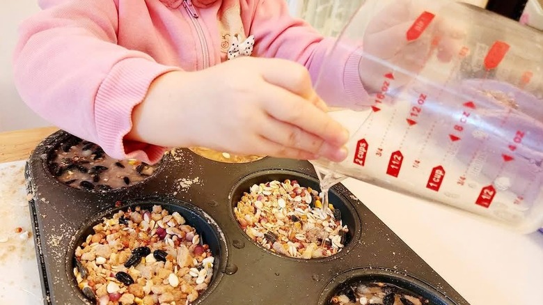 A child adding bird seed and liquid to a muffin tin