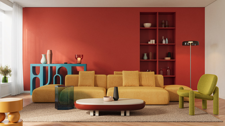 A color-drenched living room with a red wall, mustard sofa, green chair and blue console table