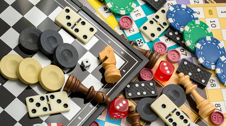 Dice, dominoes, poker chips, and chess pieces all layed out together on a messy table