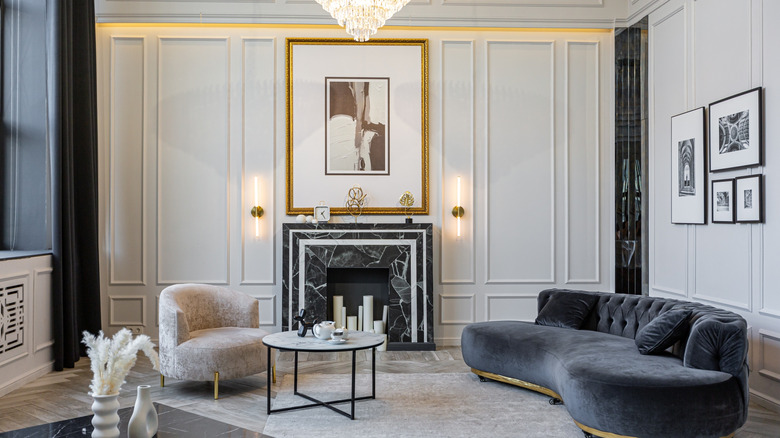Stately living room with rounded gray velvet sofa, tall ceilings and a black and white marble fireplace