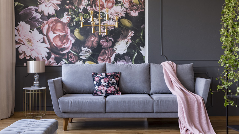 A living room with a bold floral wallpaper on the wall and a matching accent pillow on a gray sofa