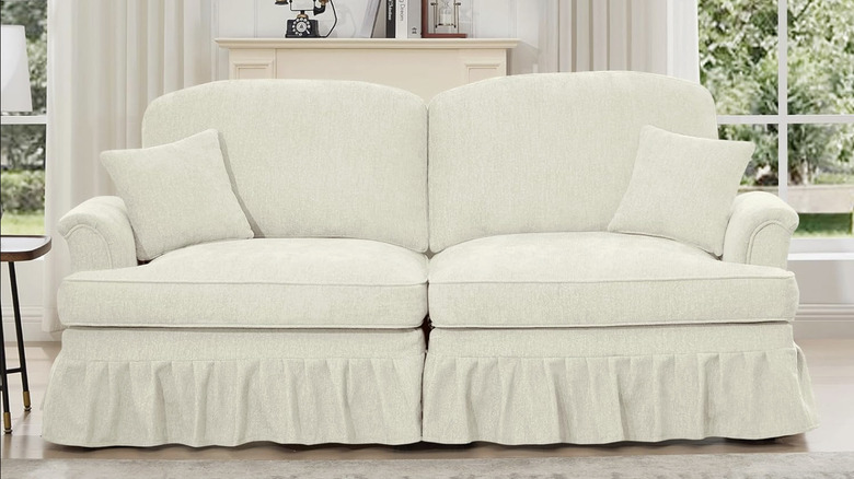 A traditional sofa in white with a curvy back and ruffles along the bottom in a white living room