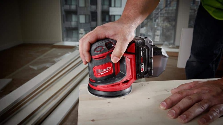 Person using sander on wooden plank