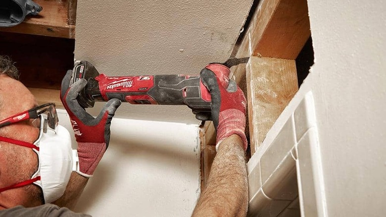 Person cutting drywall with an oscillating multi-tool