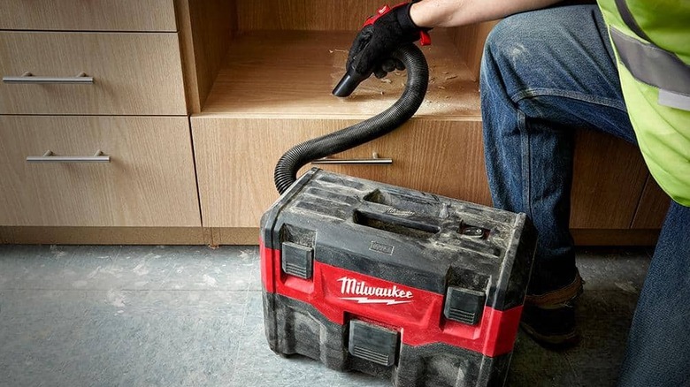Person using wet dry vacuum to remove sawdust from furniture
