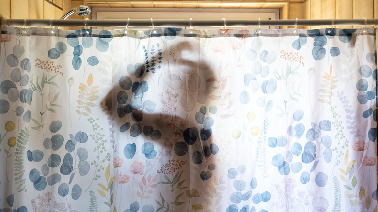 Silhouette of a person in the shower, behind a floral shower curtain.