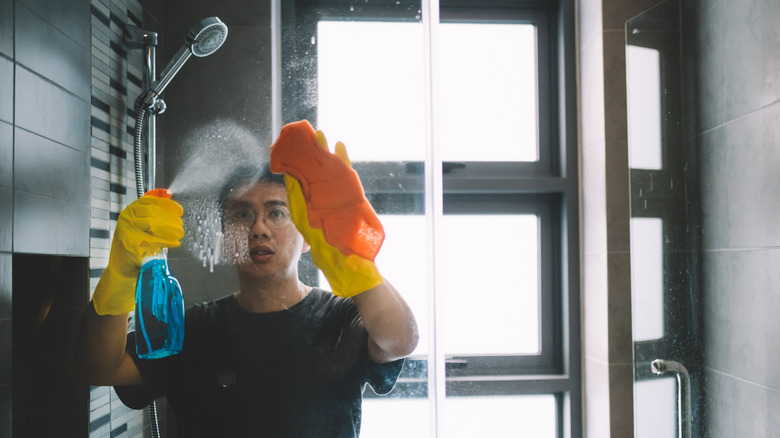 Young man cleaning glass shower door in bathroom