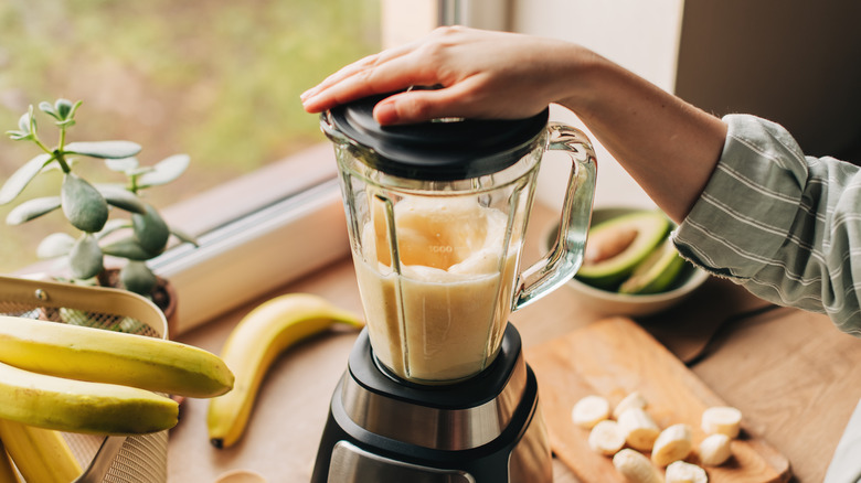 A person's hand on the lid of a blender as it's in the process of blending a smoothie.
