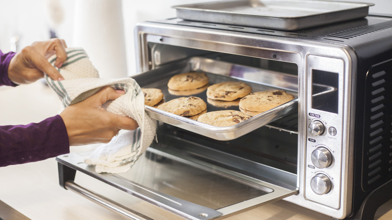 Person removing a tray of cookies from a stainless steel countertop oven