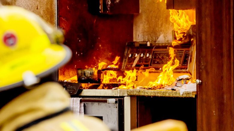 A firefighter standing outside a kitchen that's engulfed in flames.