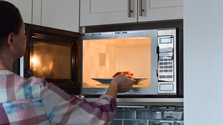 Woman putting a plate of food into a wall-mounted microwave
