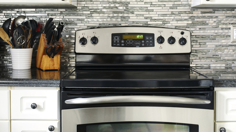Kitchen with a stainless steel and black electric range, gray backsplash, and white cabinets.