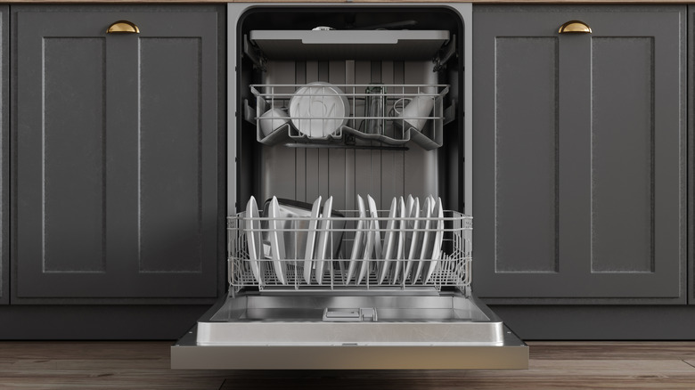 An open dishwasher with clean white dishes tucked between dark gray cabinets.