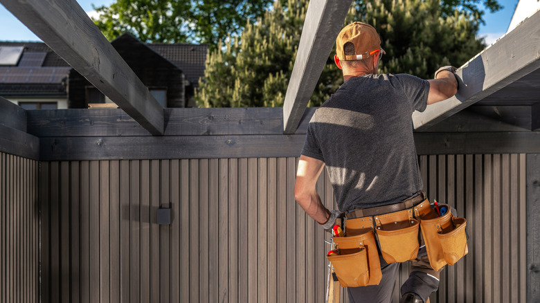 A contractor stands on a ladder as he builds a pergola