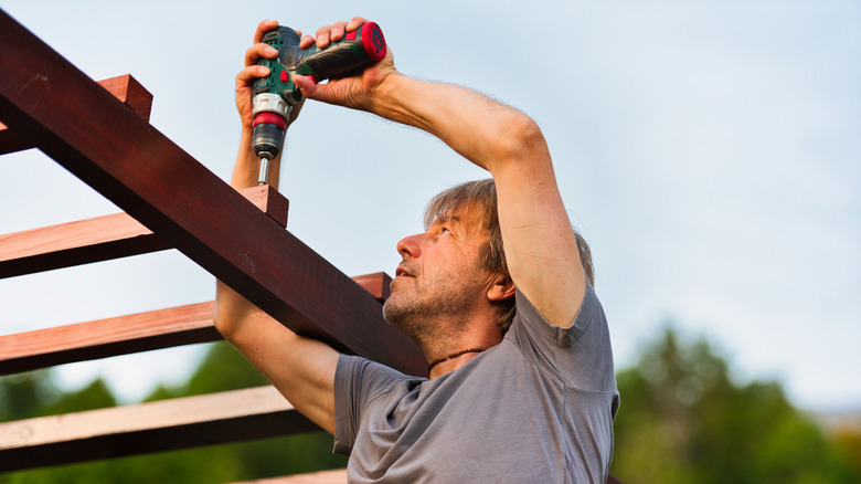 A man fixing the top beams on a pergola