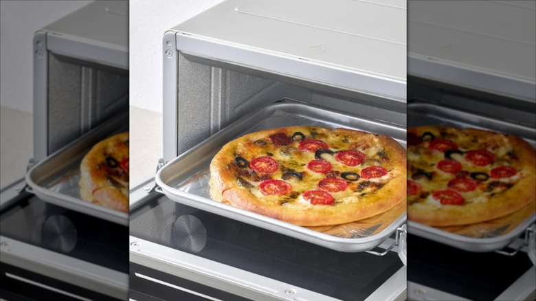 Costco's countertop toaster oven with pizza being put on tray to cook.