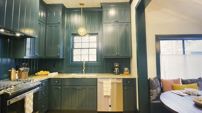 Wood paneled small kitchen with deep green cabinets and paneled walls.