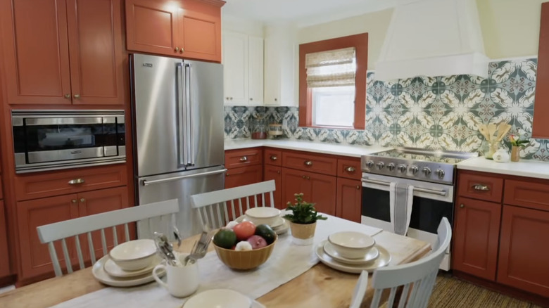 Kitchen with rust-colored cabinetry, stainless appliances, and an intricate geometric tile backsplash.