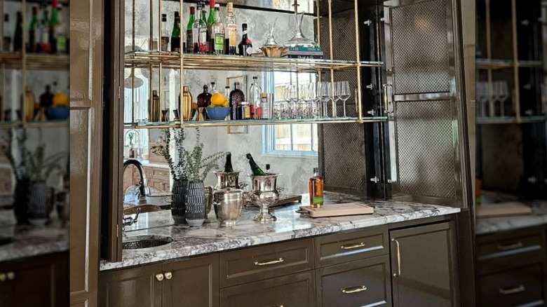 A wet bar with shelving in front of antique mirrored backsplash.