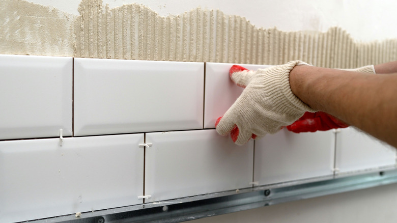 Gloved hand pressing a rectangular tile on the wall while installing a backsplash