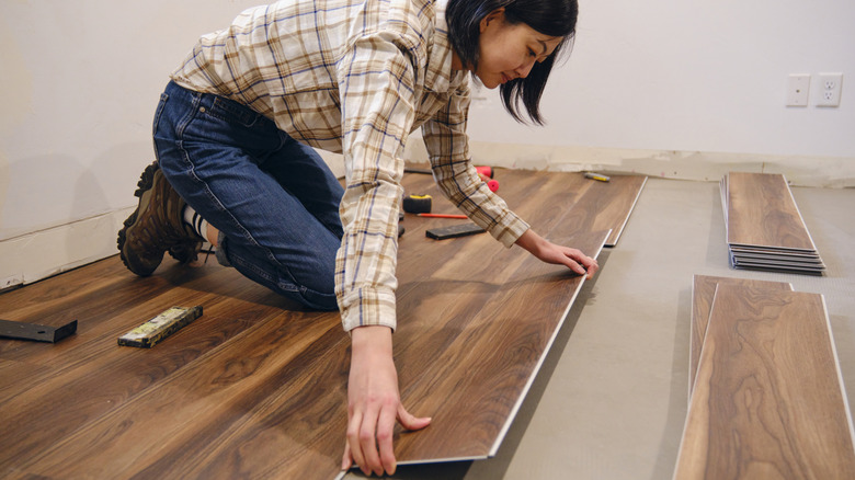 A woman installing laminate flooring in a home