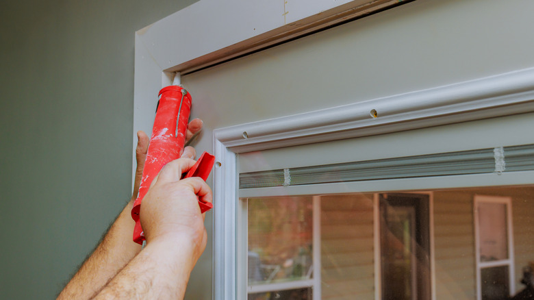 Applying caulk along a window frame to seal gaps