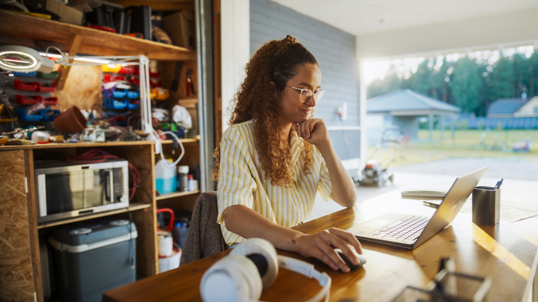 Young woman browsing laptop in garage filled with tools