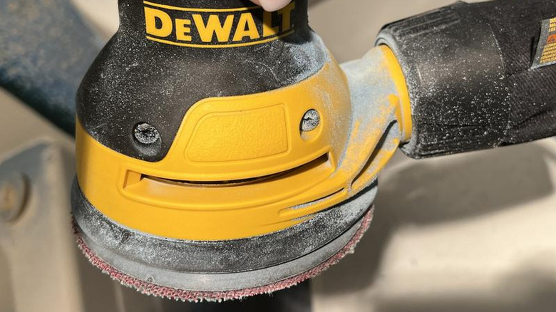 Close-up of DeWalt orbital sander with sandpaper and dust