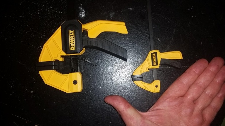 Large and small DeWalt trigger clamps side by side on black surface beside hand for reference