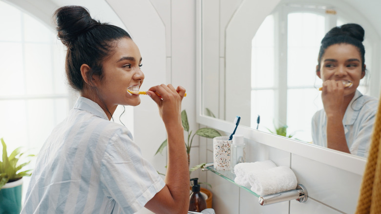 Young woman brushing her teeth in front of bathroom mirror