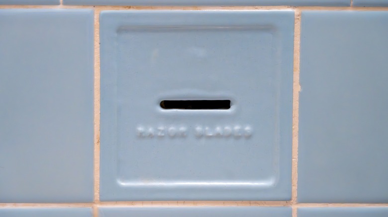 A vintage razor blade disposal slot built into a bathroom wall