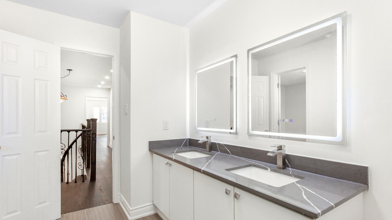 Beautiful white bathroom with dark countertops and backlit mirrors