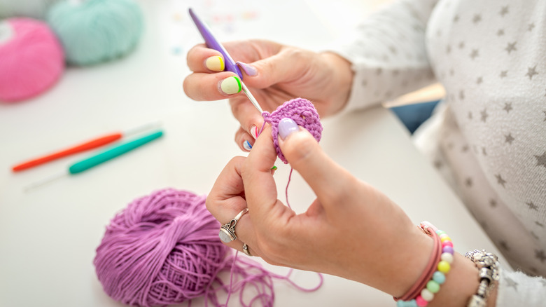 A woman crochets using purple yarn.