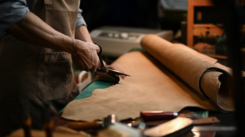 A person wearing a blue shirt and brown apron cuts a roll of kraft paper with scissors.