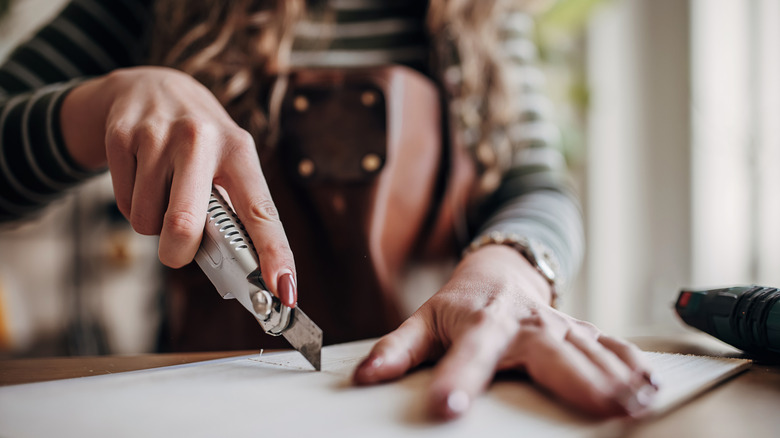 A woman in a brown apron uses a blade to cut a craft.