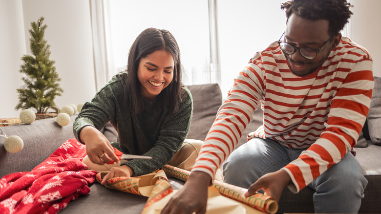 A couple smiles as they cut wrapping paper for gifts.