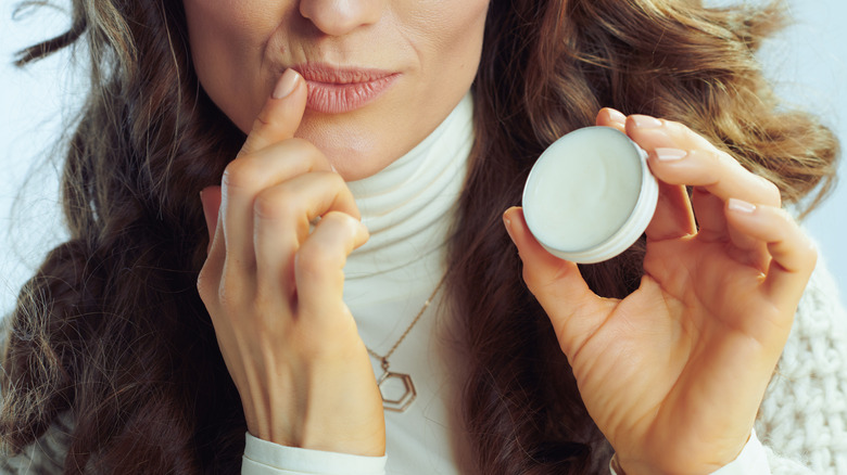 A woman in a white turtleneck applies lip balm to her lips.
