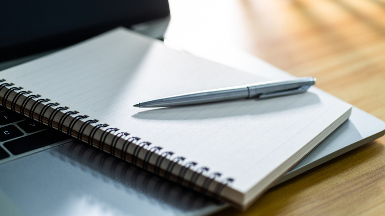 A pen and blank notebook sit on top of an open laptop.