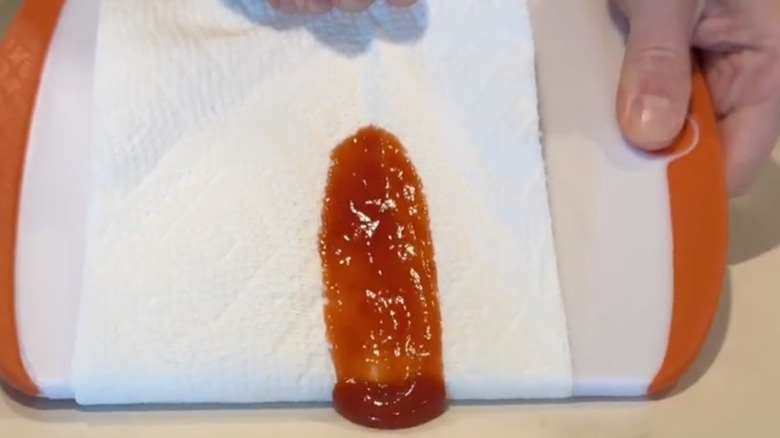 person picking up ketchup spill with paper towel hack