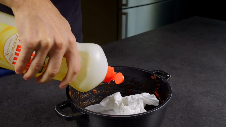 person placing dish soap and crumpled paper towels in a dirty pasta pot